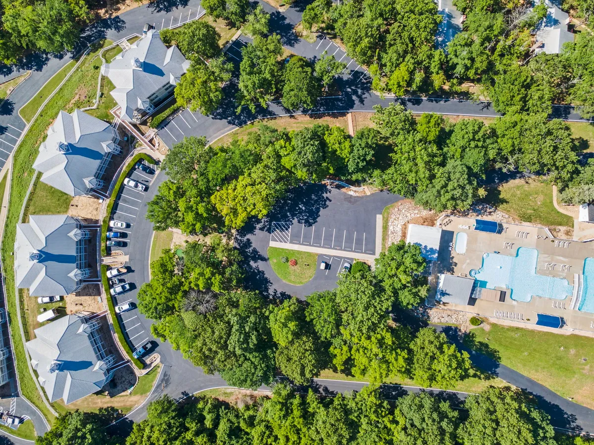 A sparkling outdoor swimming pool surrounded by lush greenery and the condo building in the background. Lounge chairs are set up for relaxing, and the area evokes a sense of summertime leisure and social gatherings.