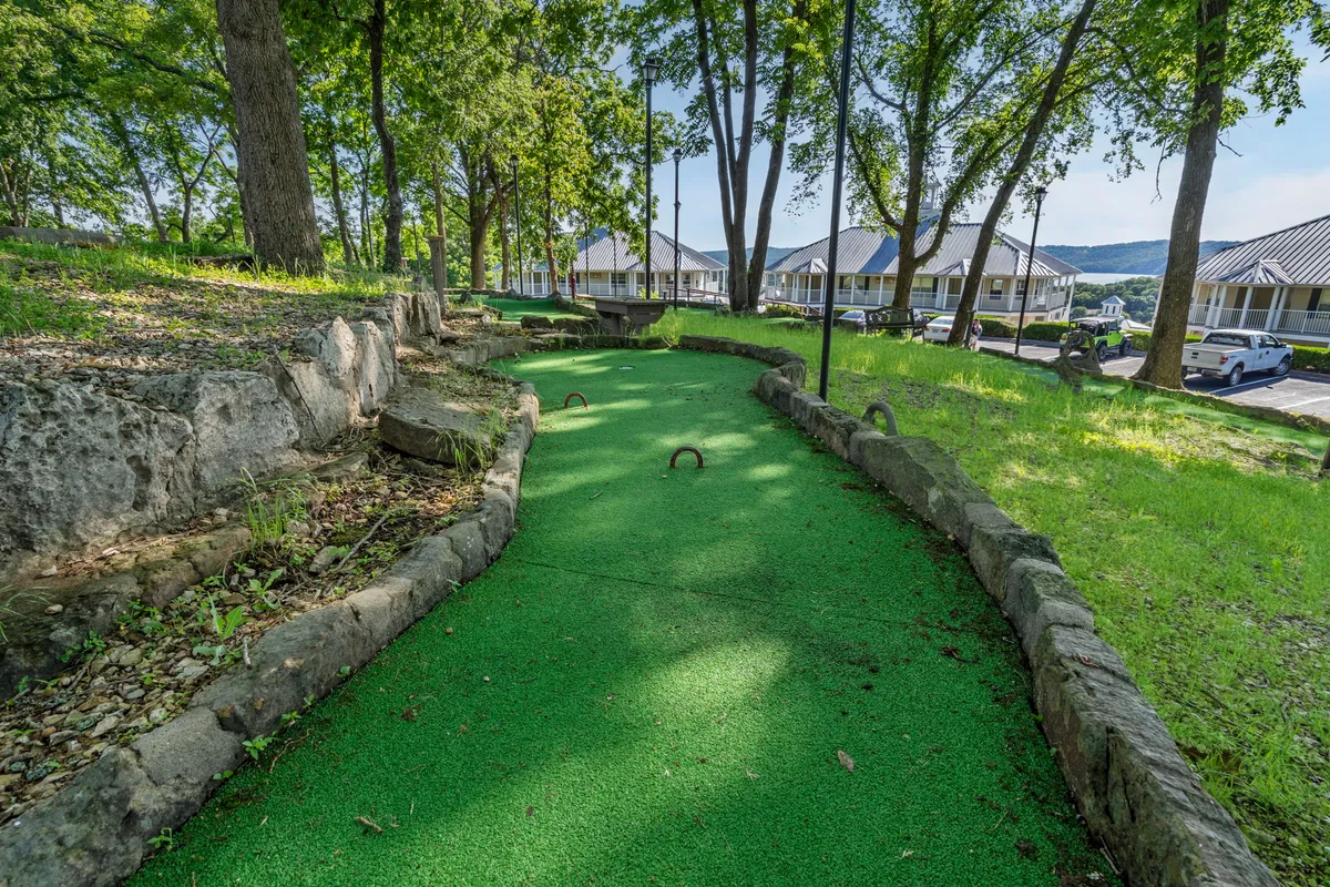 A playful exterior view of a mini-golf course surrounded by trees and stone pathways. The scene invites friendly competition and group fun, with natural elements creating a cheerful, relaxed backdrop for families or friends to gather and enjoy resort amenities.