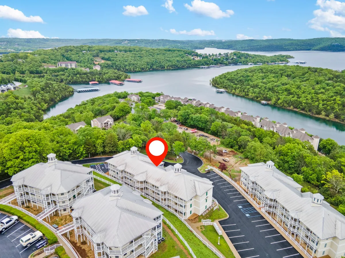 A tranquil exterior shot showing Table Rock Lake framed by lush greenery, with residential buildings visible in the background. The image suggests activities such as boating, hiking, or simply relaxing by the water, and hints at the scenic natural setting around the condo.