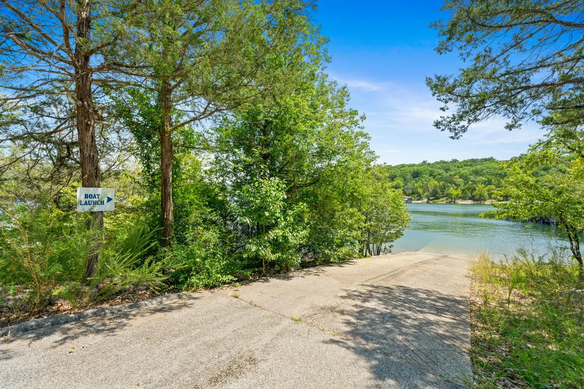 A concrete boat ramp leads directly into the sparkling waters of Table Rock Lake, surrounded by lush greenery. A clearly marked 'boat launch' sign sits at the entrance, making the purpose of the space unmistakable. The gentle slope of the ramp and tranquil lake setting suggest easy access for boats and kayaks, inviting visitors to embark on water adventures.
