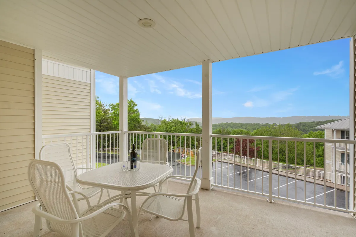 A tranquil outdoor table with chairs and a bottle of wine, set against a scenic lakeside view. The vantage point suggests an elevated balcony or patio, capturing the serenity of the water and sky beyond.