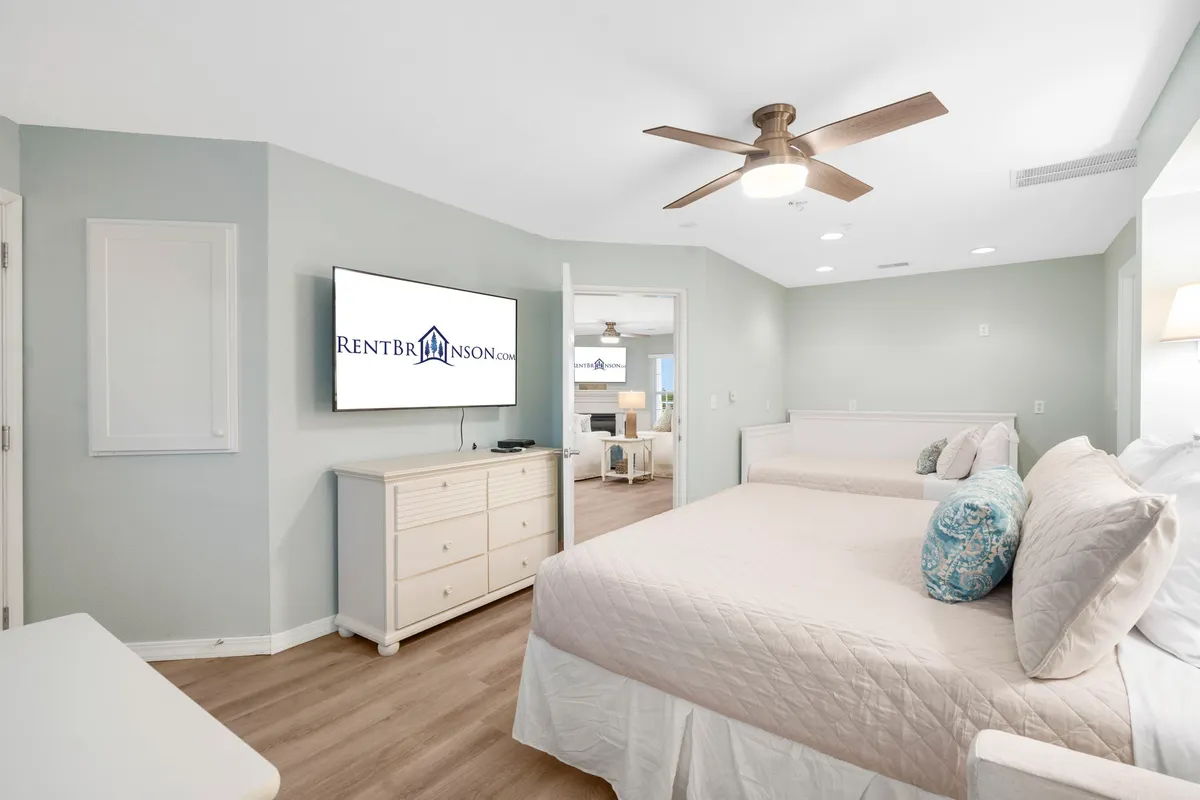 A cozy bedroom featuring two beds with decorative pillows, a wall-mounted TV, and a functional dresser — an inviting setup for families or groups seeking a flexible sleeping arrangement.