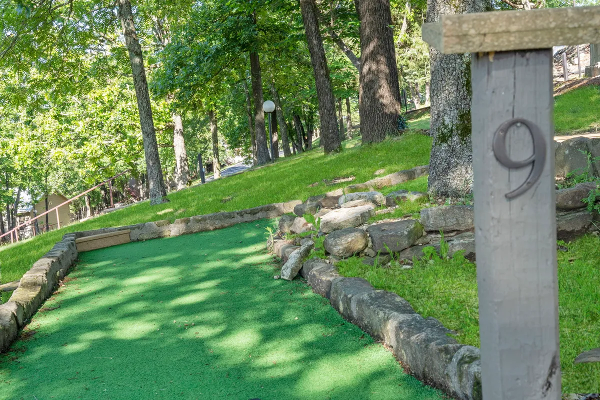 A vibrant mini-golf course set amidst greenery and stone pathways. The green features a numbered post and is designed for easy access, surrounded by a cheerful, playful environment that encourages family participation and fun.