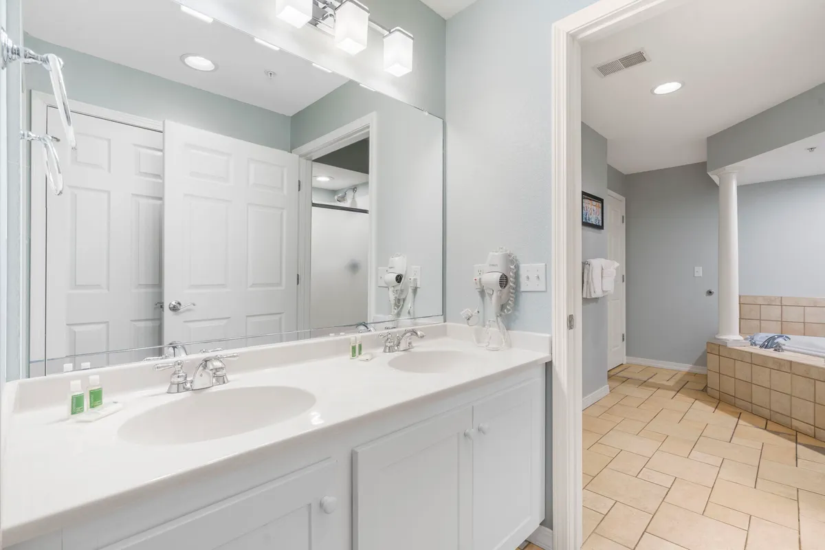 A modern, well-organized bathroom with a double sink vanity, a bathtub with a shower combo, and elegant light fixtures. The space is bright, serene, and ideal for both quick routines and long, relaxing soaks.