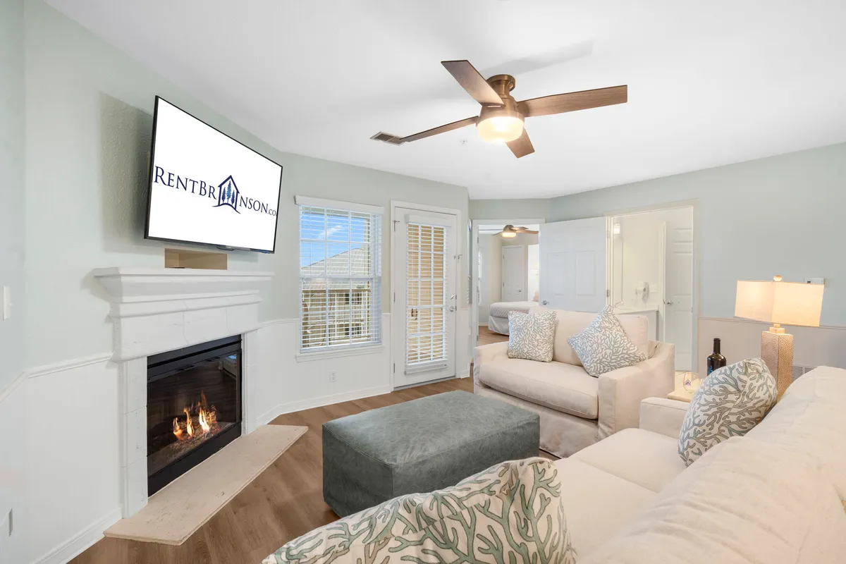 A warm, inviting living room featuring a stone fireplace, comfortable sofa, ottoman, and a television. The space radiates coziness, perfect for relaxing evenings, family game nights, or unwinding after a day at Table Rock Lake.