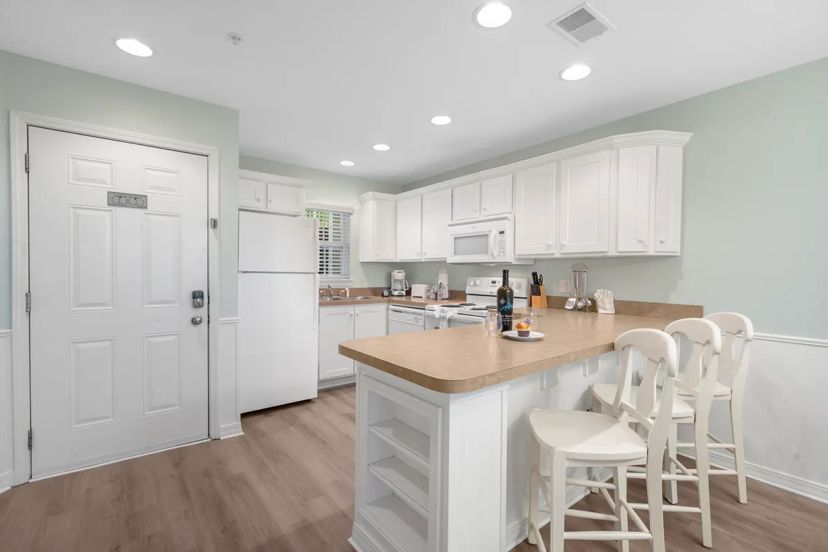A warmly lit kitchen featuring a central island with stools, modern appliances, and ample cabinetry. The space feels open and inviting, perfect for group cooking sessions or casual breakfasts. The arrangement encourages social interaction and easy movement, making it ideal for family gatherings or entertaining.