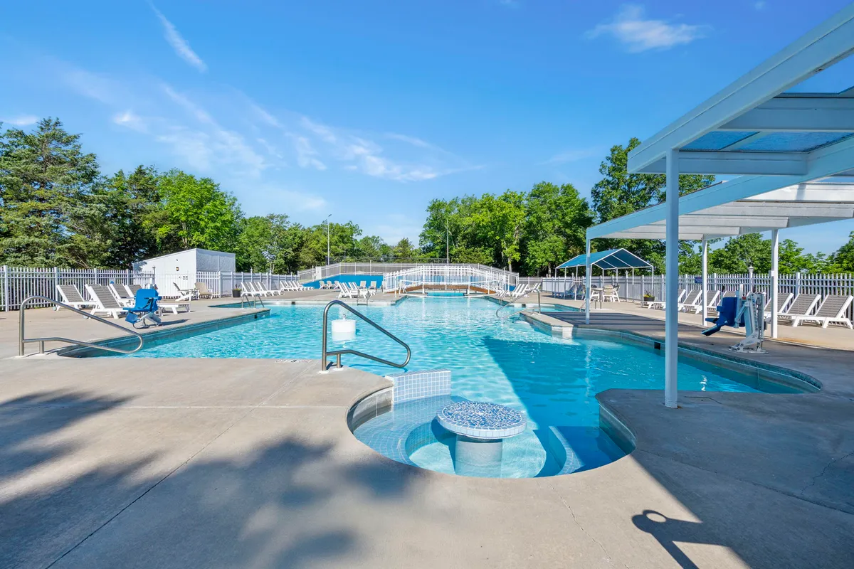 A beautifully landscaped outdoor swimming pool area featuring a pool, hot tub, and rows of lounge chairs set amid gardens. The area is inviting for both relaxation and socializing.