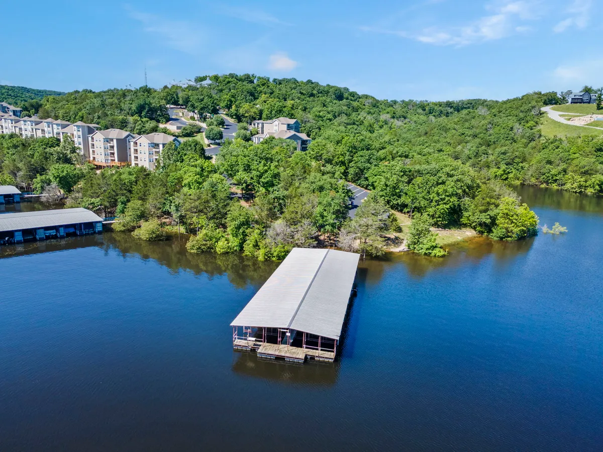A peaceful lakeside scene featuring a boat dock, calm water, and surrounding greenery with residential buildings visible. The setting is ideal for boating, fishing, or simply enjoying the waterfront.